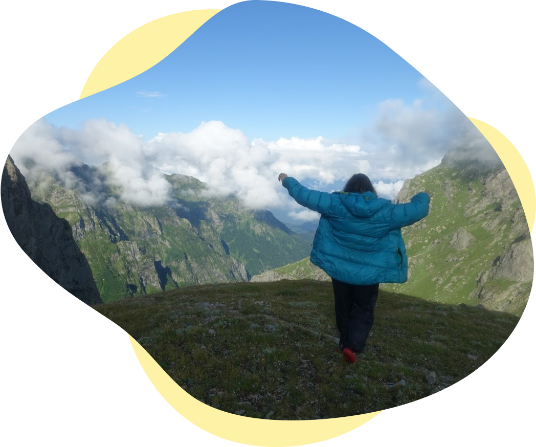 Meg raising arms walking away from camera surrounded by mountain tops