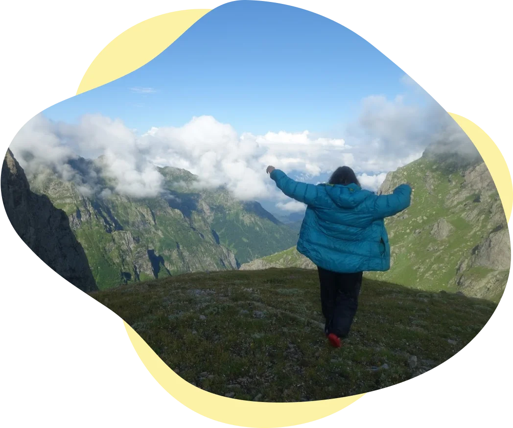 Meg raising arms walking away from camera surrounded by mountain tops